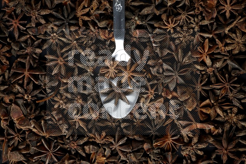 Star Anise in a metal spoon on more stars anise filling the frame on black flooring
