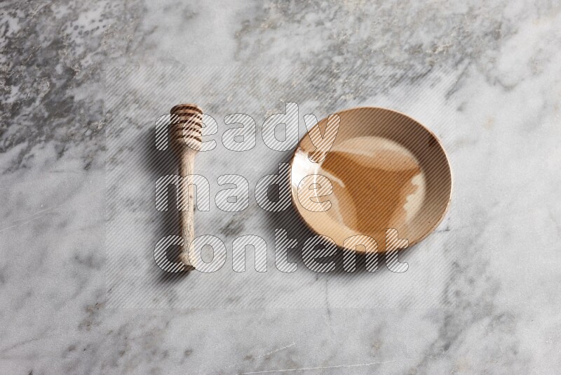 Multicolored pottery plate with wooden honey dipper on the side on grey marble background