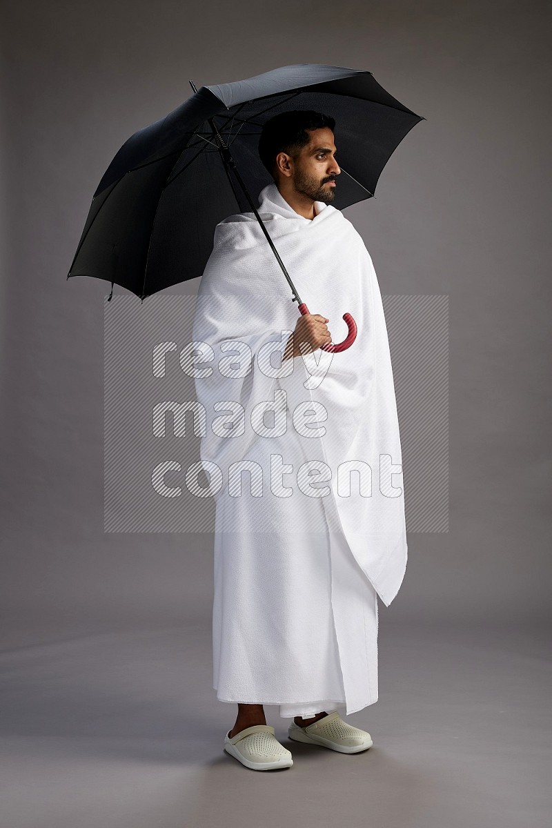 A man wearing Ehram Standing holding umbrella on gray background