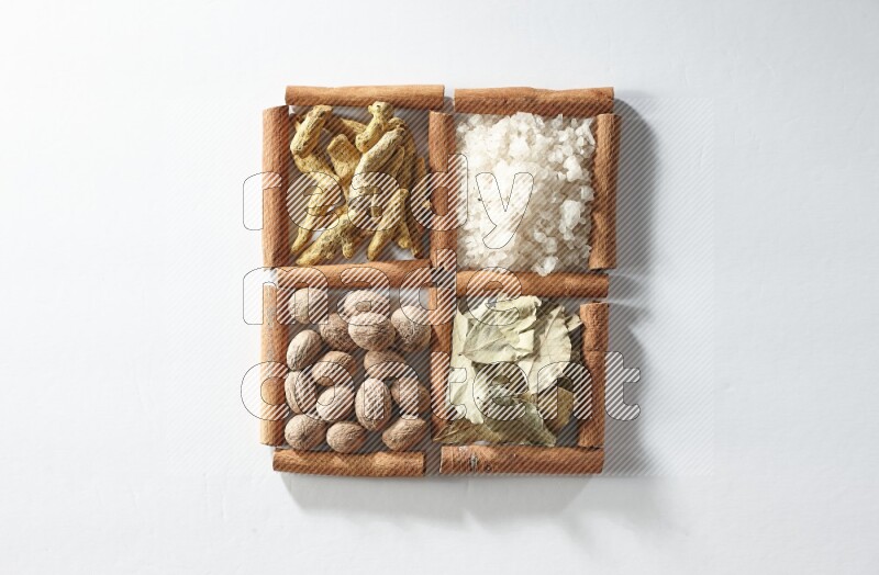 4 مربعات من أعواد القرفة ممتلئة بالملح وورق الغار وجوزة الطيب والكركم على أرضية بيضاء