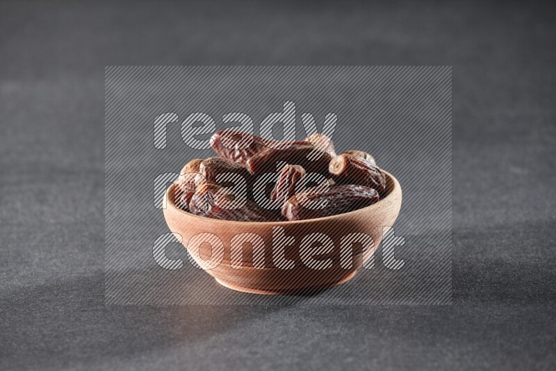 A wooden bowl full of dried dates on a black background in different angles