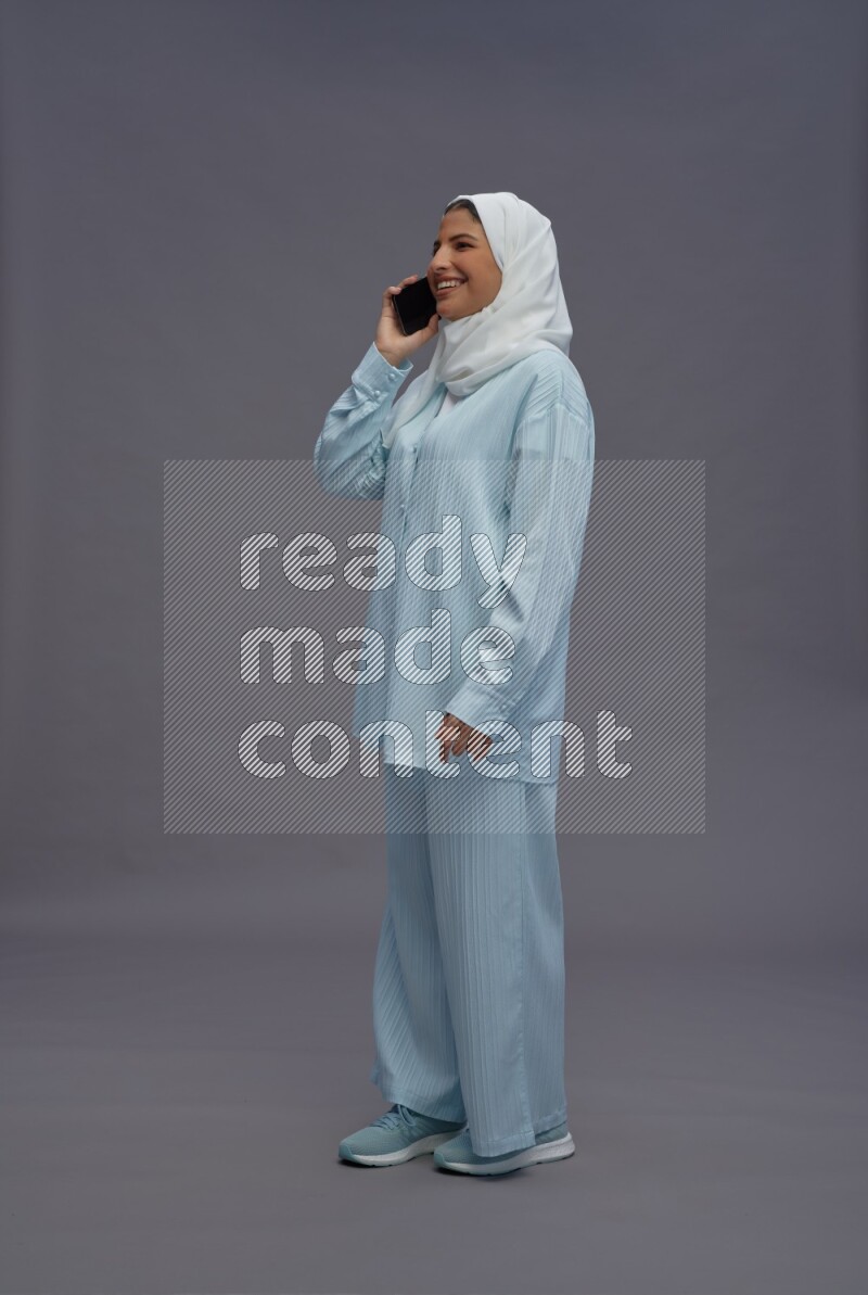 Saudi woman wearing hijab clothes standing talking on phone on gray background