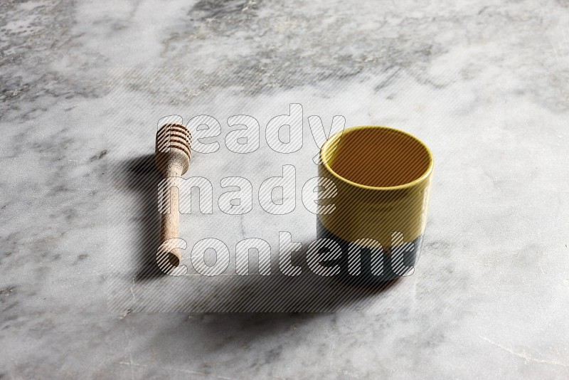 Multicolored Pottery cup with wooden honey handle on the side with grey marble flooring, 45 degree angle