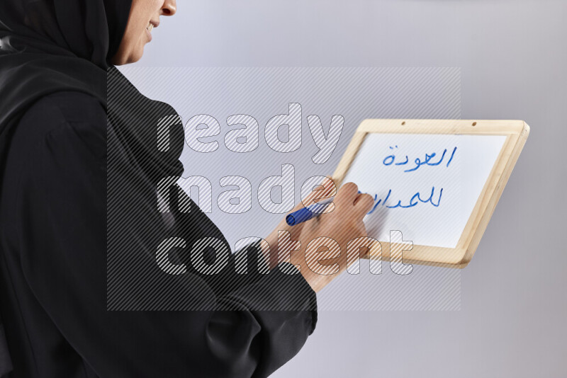 A woman in abaya holding books and a board in different positions (back to school)