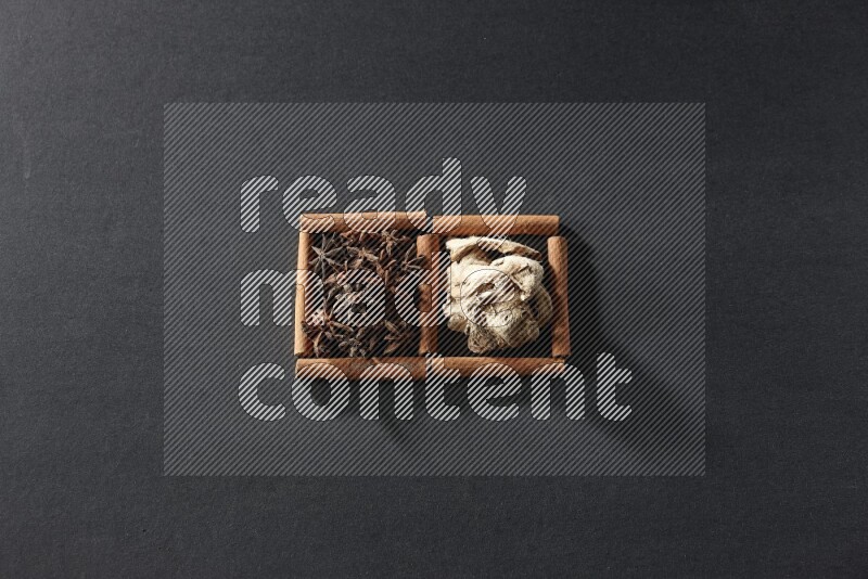 مربعان من أعواد القرفة ممتلئان باليانسون النجمي والزنجبيل المجفف علي خلفية سوداء