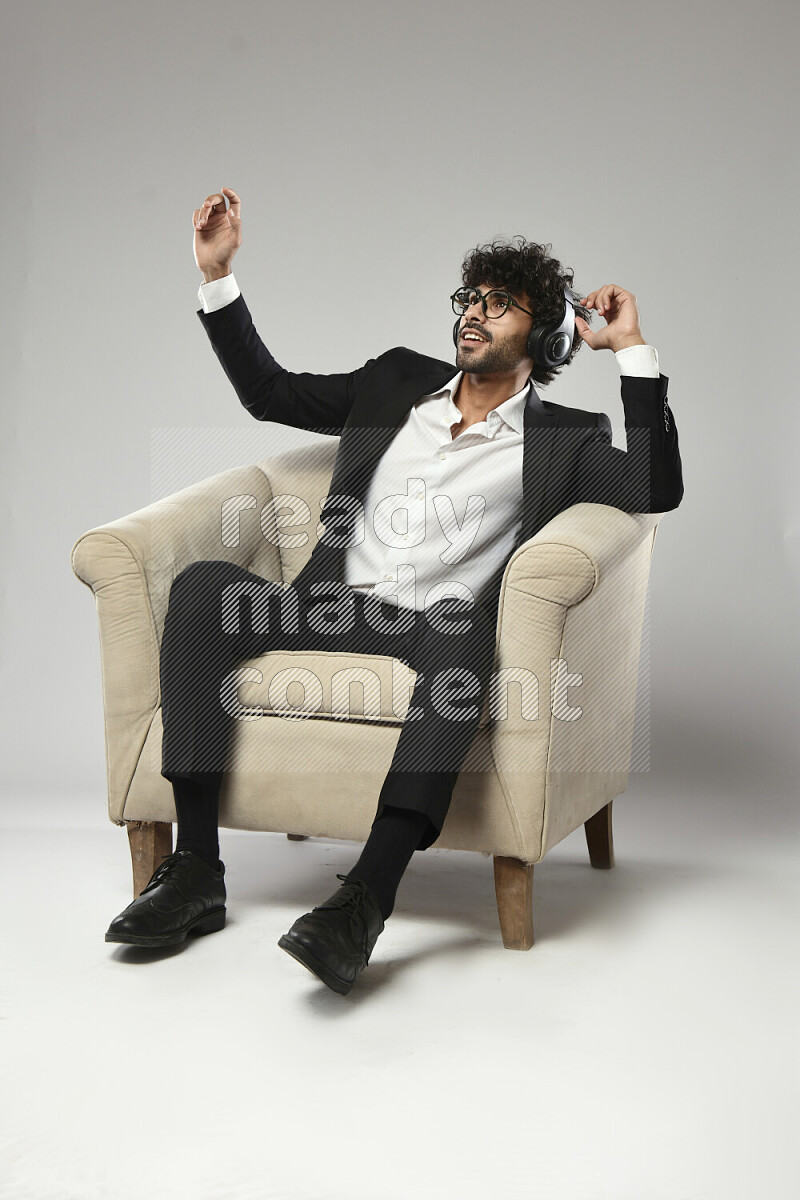 A man wearing formal sitting on a chair putting on headphones on white background