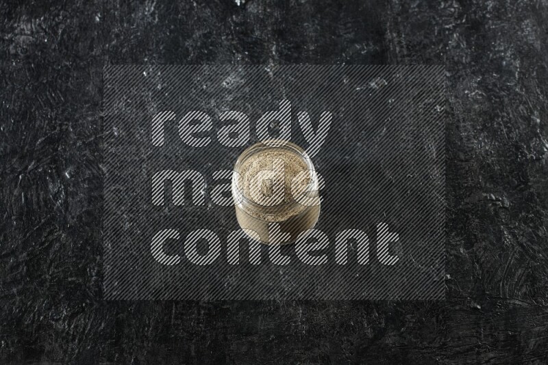 وعاء زجاجي ممتلئ ببودرة الهيل على خلفية سوداء