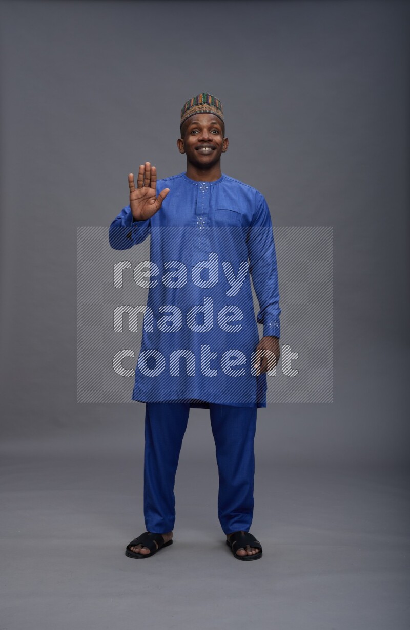Man wearing Nigerian outfit standing interacting with the camera on gray background