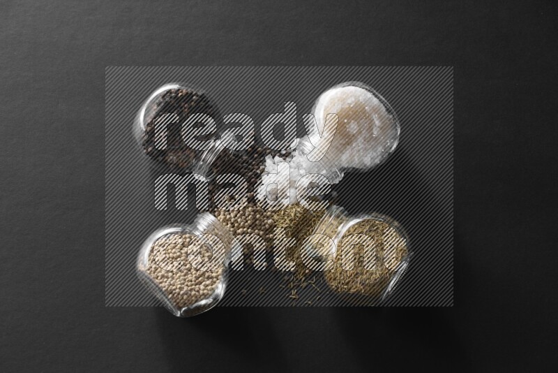 ملح وفلفل أسود وفلفل أبيض وكمون في أوعية زجاجية علي خلفية سوداء