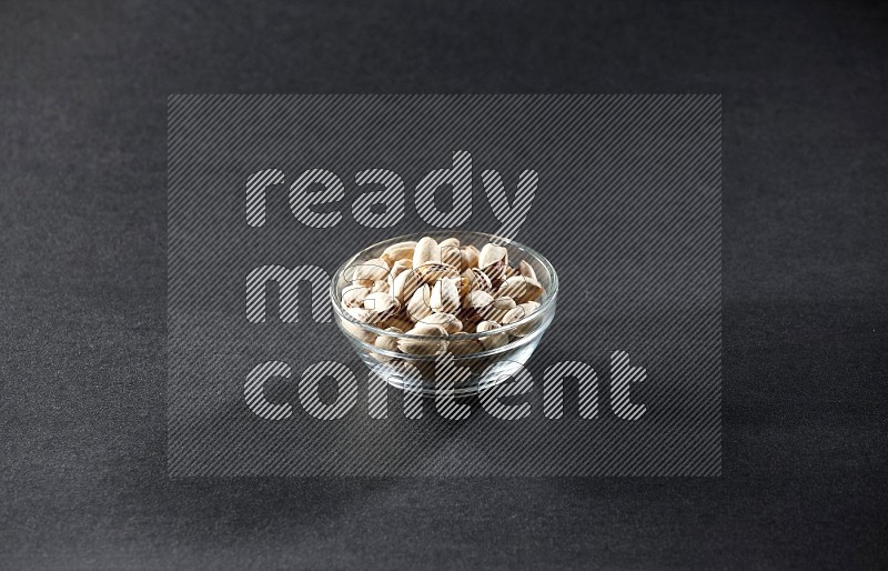 A glass bowl full of pistachios on a black background in different angles