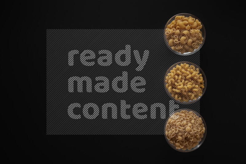 Different pasta types in 3 glass bowls on black background