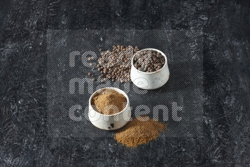 2 beige bowls, one full of allspice powder and the other full of whole balls and both spread on a textured black flooring