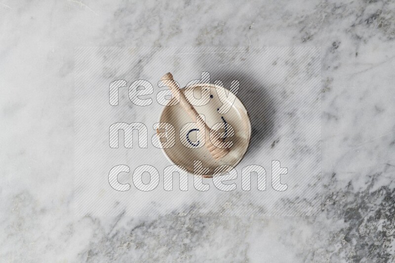 Multicolored pottery bowl with wooden honey dipper in it on grey marble background