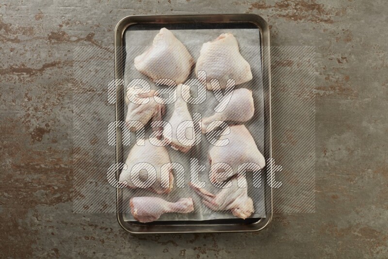 Mixed fresh chicken pieces in an oven tray on a textured rustic background