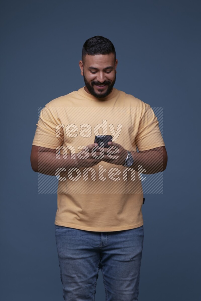 A man Texting on his phone on Blue Background wearing Orange T-shirt
