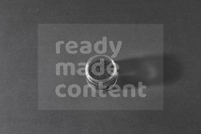 وعاء زجاجي ممتلئ ببذور حبة البركة علي خلفية سوداء