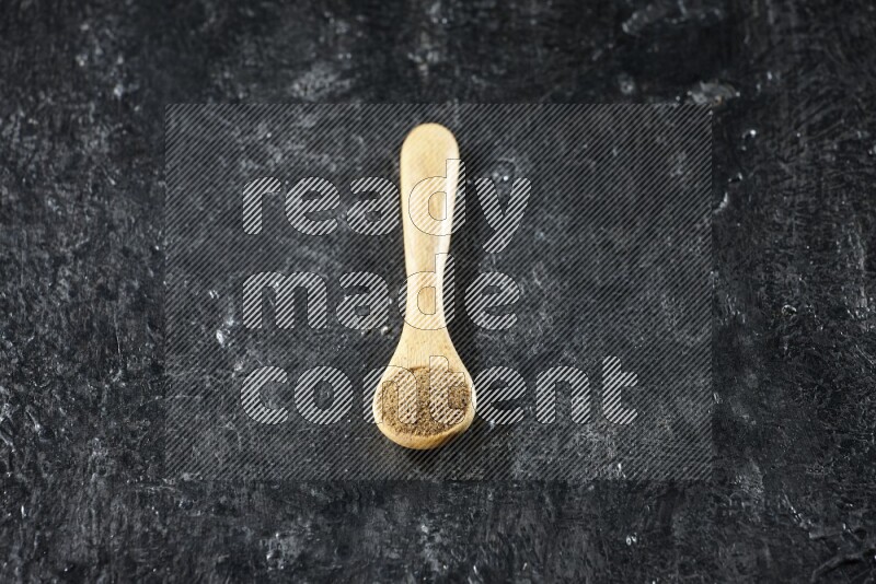 ملعقة خشبية ممتلئة ببودرة الكمون على خلفية سوداء