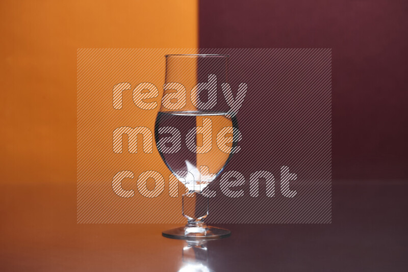 تظهر الصورة أواني زجاجية ممتلئة بالماء موضوعة على خلفية من اللونين البرتقالي والأحمر الغامق