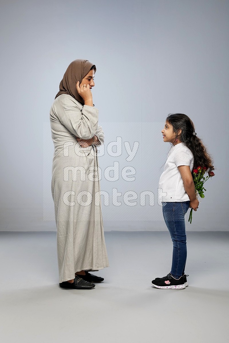 A girl standing giving flowers to her mother on gray background