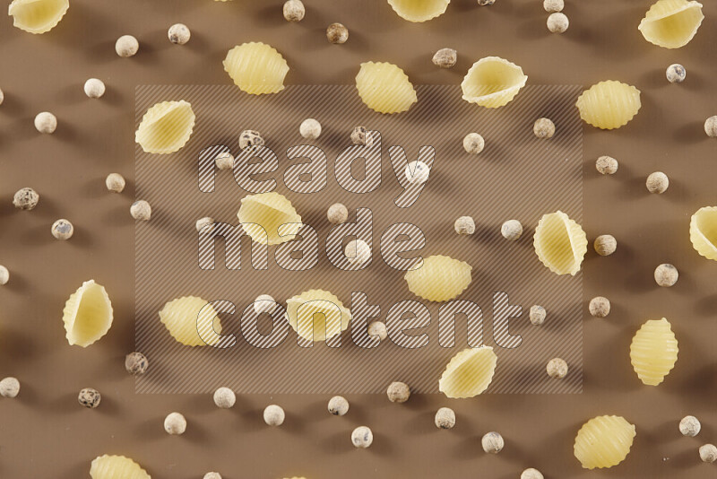 Raw pasta with different ingredients such as cherry tomatoes, garlic, onions, red chilis, black pepper, white pepper, bay laurel leaves, rosemary and cardamom on beige background