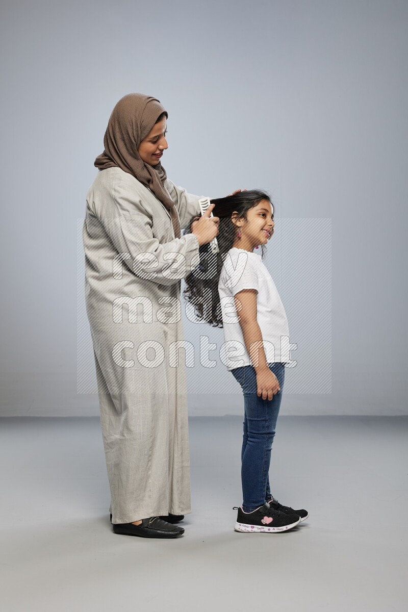 Mom standing styling hair for her daughter on gray background