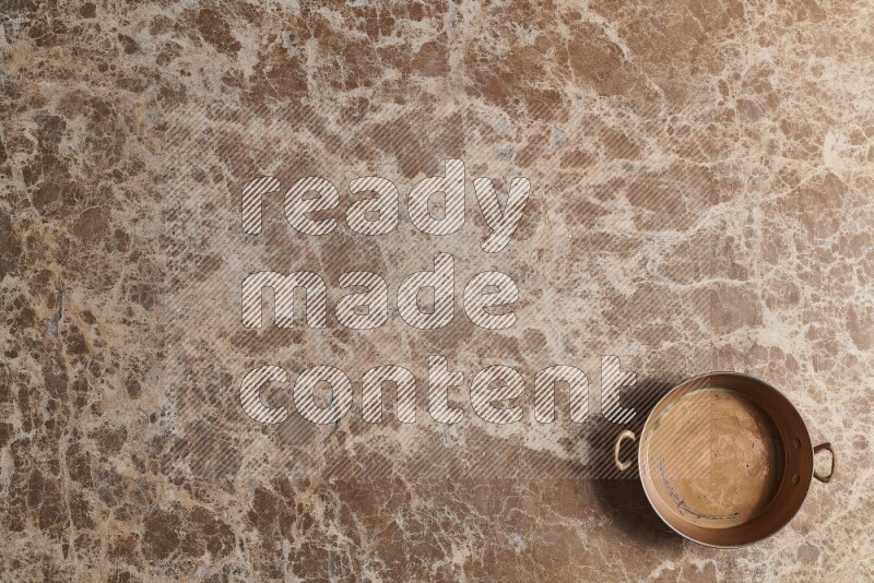 A small copper pan on beige marble background