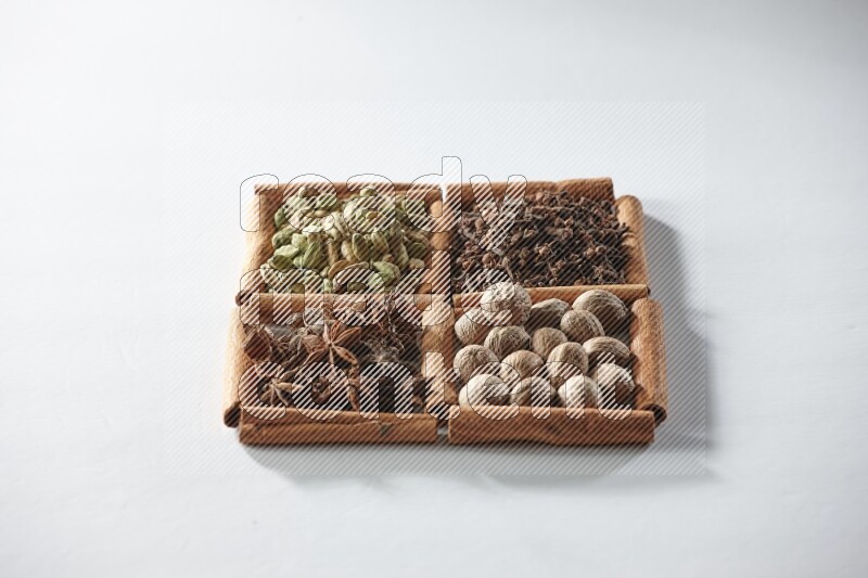 4 مربعات من أعواد القرفة ممتلئة بالهيل واليانسون والقرنفل وجوزة الطيب على أرضية بيضاء