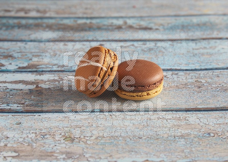 45º Shot of of two assorted Brown Irish Cream, and Yellow, and Brown Chai Latte macarons  on light blue background