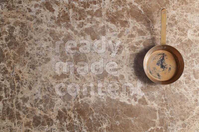 A small copper pan on beige marble background