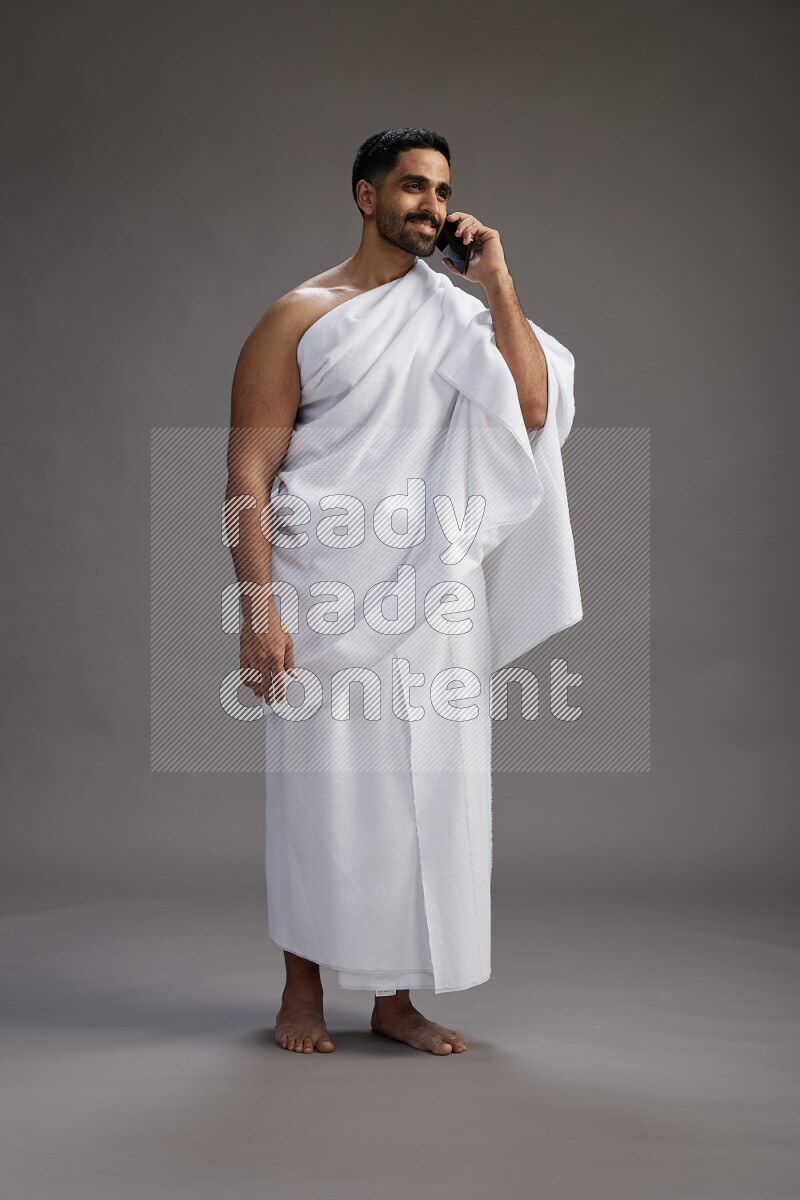 A man wearing Ehram Standing talking on phone on gray background