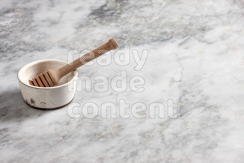 White Pottery Bowl with wooden honey handle in it, on grey marble flooring, 45 degree angle