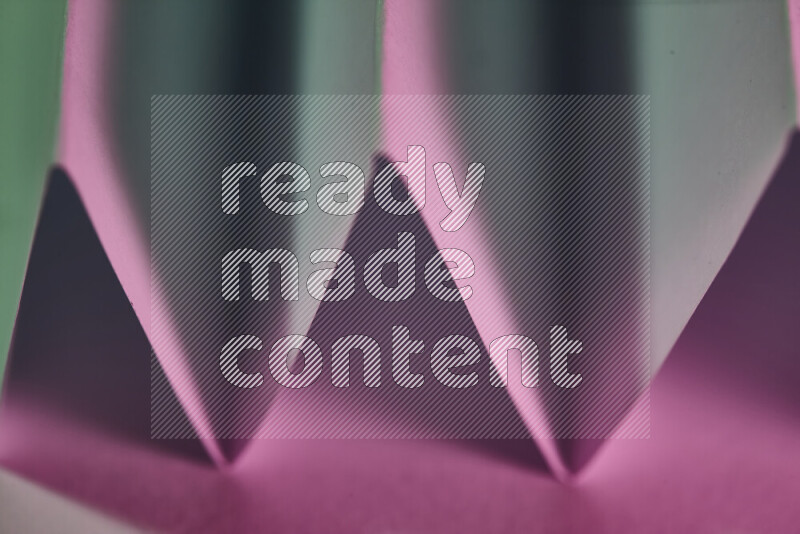 A close-up abstract image showing sharp geometric paper folds in green and pink gradients