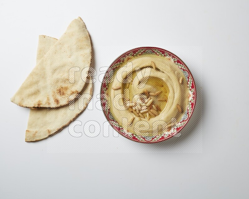 Hummus in a red plate with patterns garnished with pine nuts on a white background