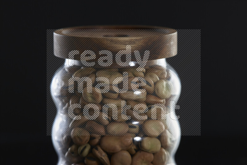 Fava beans in a glass jar on black background