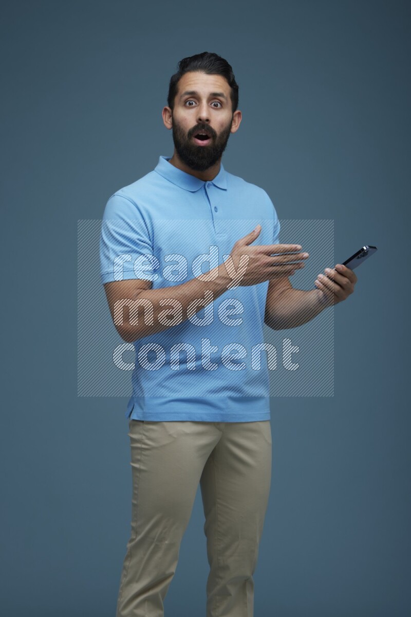 Man posing with a phone in a blue background wearing a Blue shirt