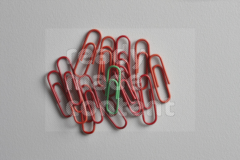 A green paperclip surrounded by bunch of red paperclips on grey background
