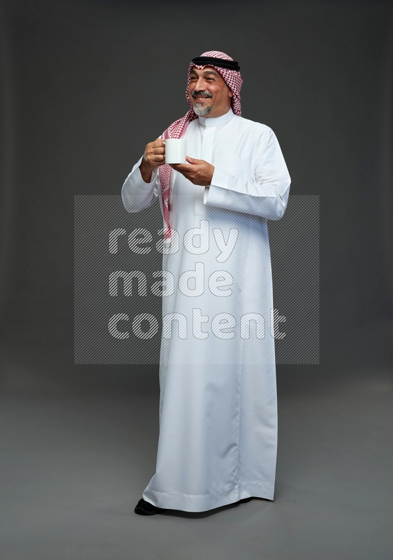 Saudi man with shomag Standing holding mug on gray background