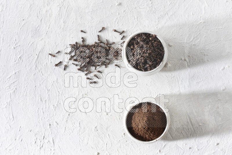 2 Beige ceramic bowls, one full of cloves and the other full of powder on textured white flooring