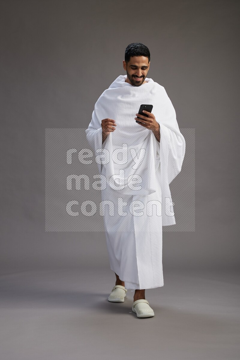 A man wearing Ehram Standing texting on phone on gray background