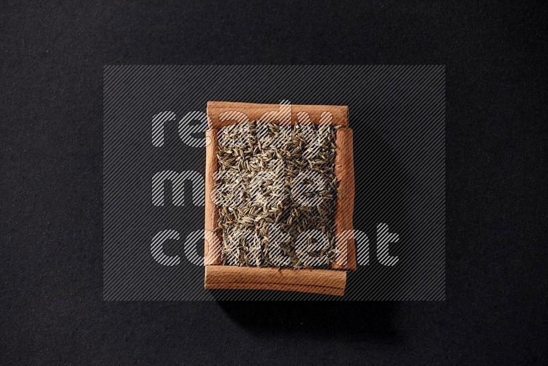 A single square of cinnamon sticks full of cumin on black flooring