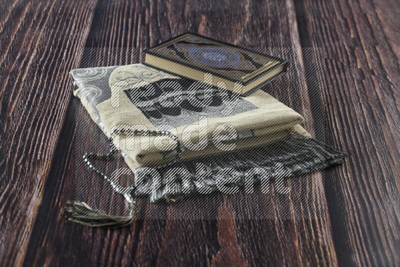 A folded prayer mat with different elements such as quran and prayer beads on brown wooden background