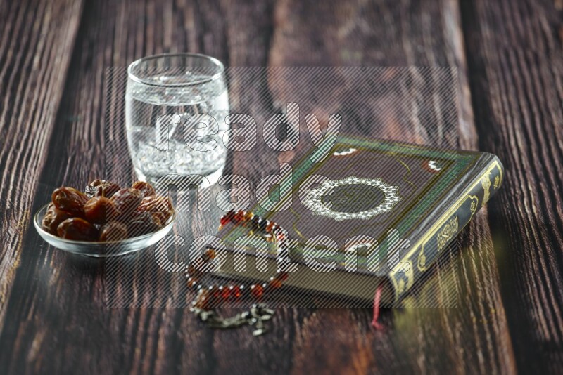 Quran with dates, prayer beads and different drinks all placed on wooden background