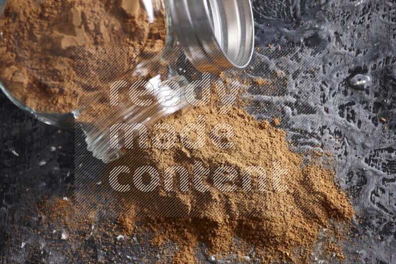 Flipped herbal glass jar full of cinnamon powder on textured black background
