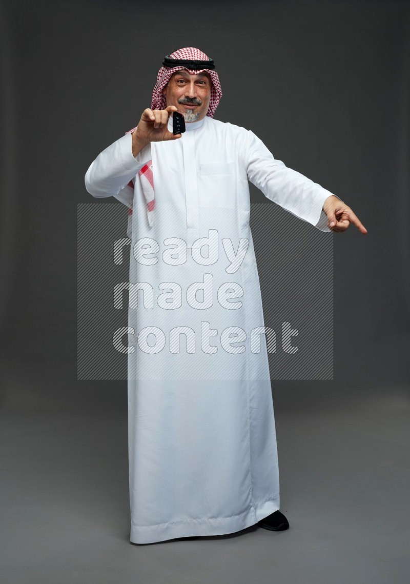 Saudi man with shomag Standing holding car key on gray background