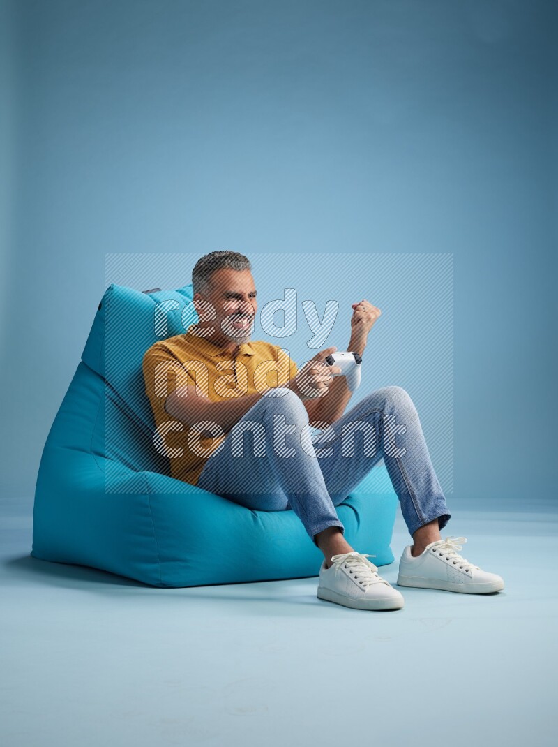 A man sitting on a blue beanbag and gaming with joystick