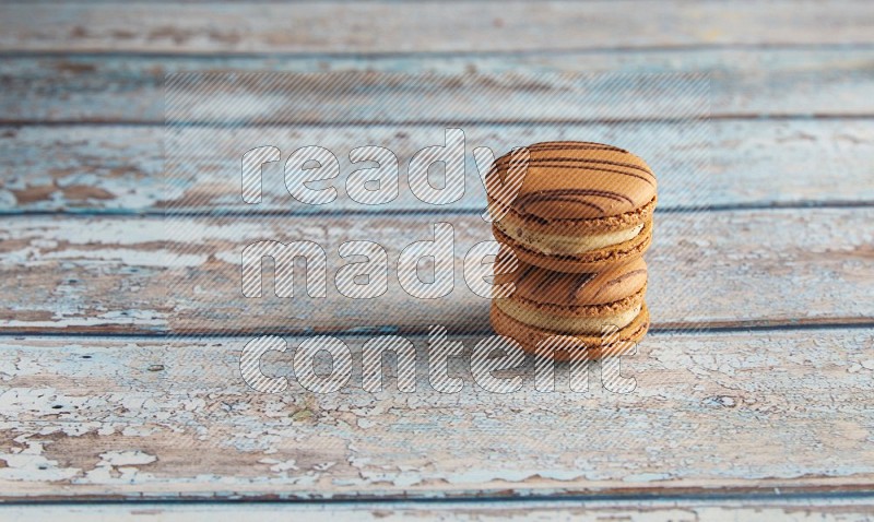 45º Shot of two light brown Almond Cream macarons on light blue wooden background