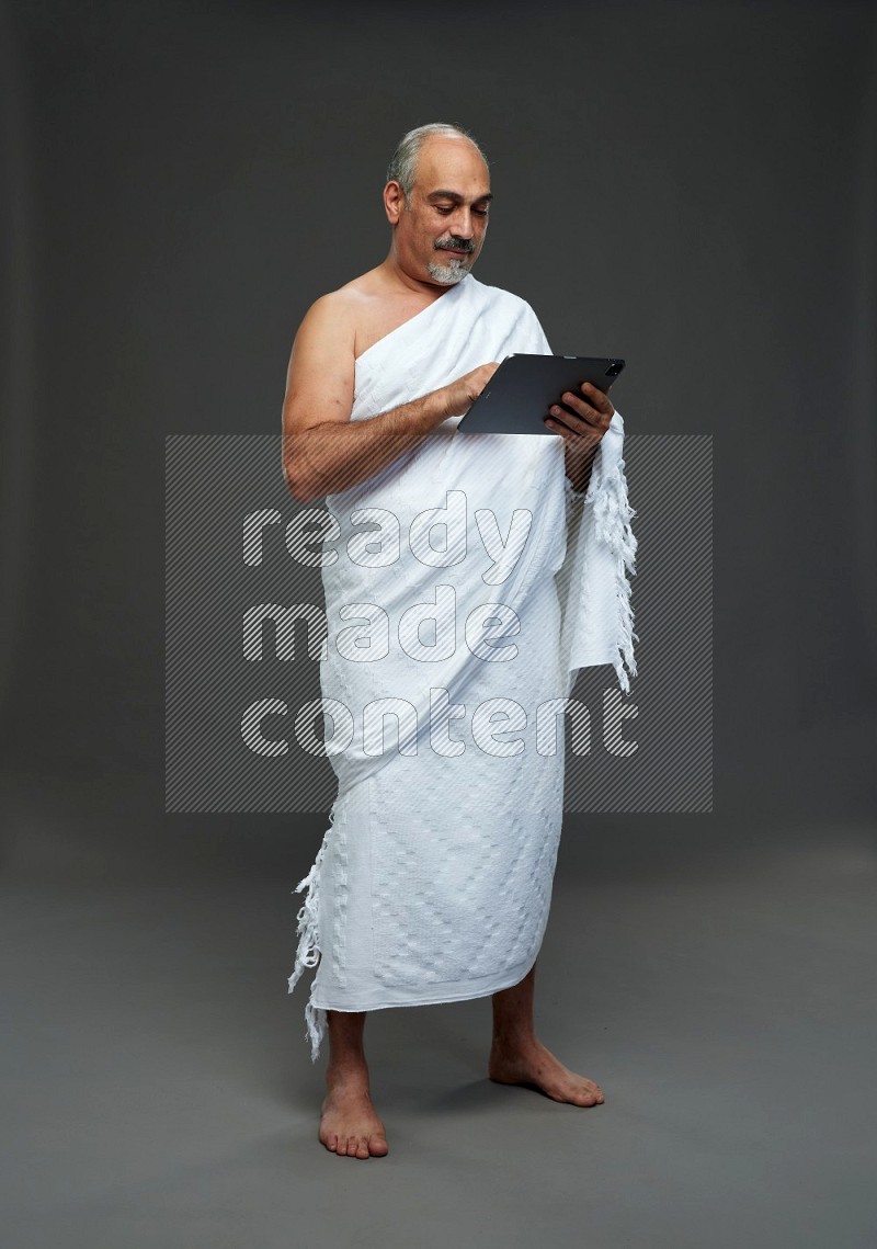 A man wearing Ehram Standing working on tablet on gray background