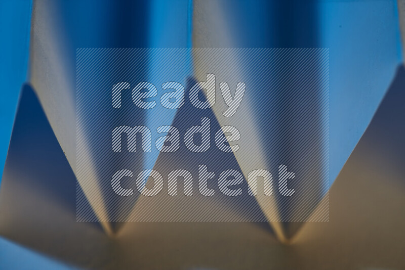 صورة مجردة مقربة تظهر طيات ورقية هندسية حادة بتدرجات اللون الأزرق مع درجات لونية دافئة