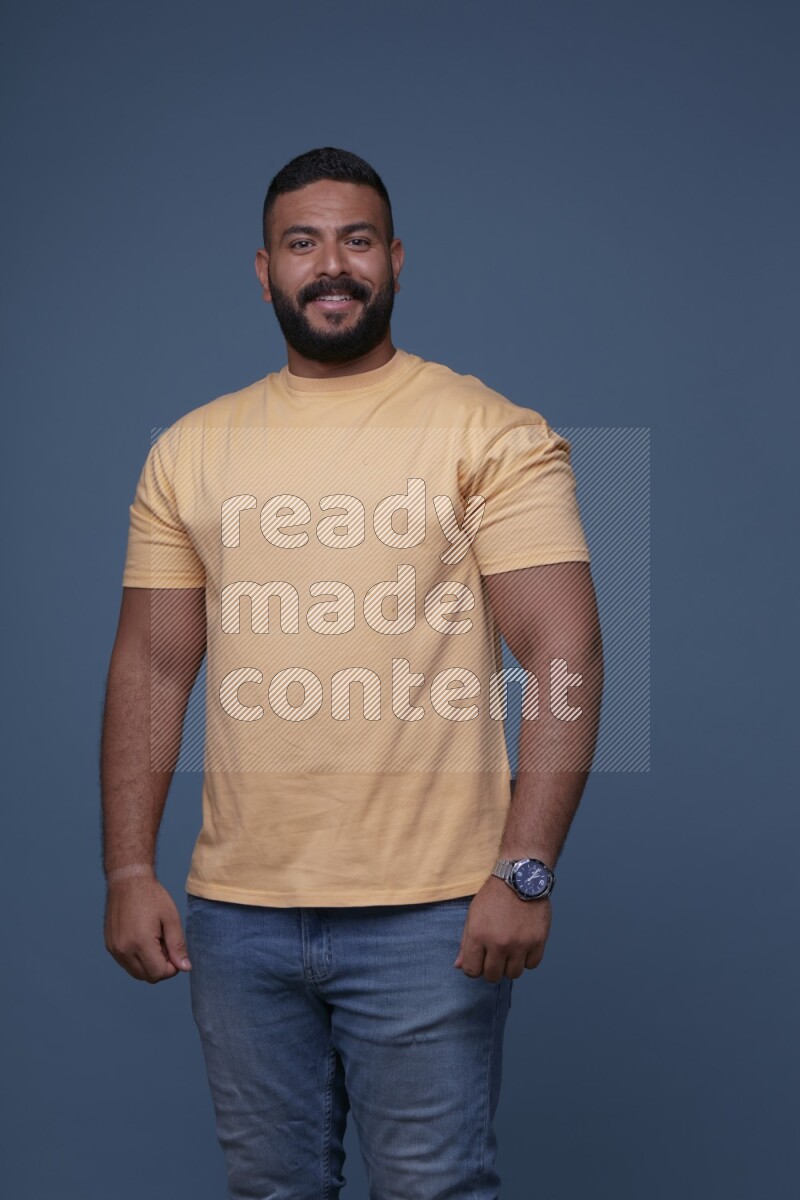 A man posing in a blue background wearing a yellow shirt