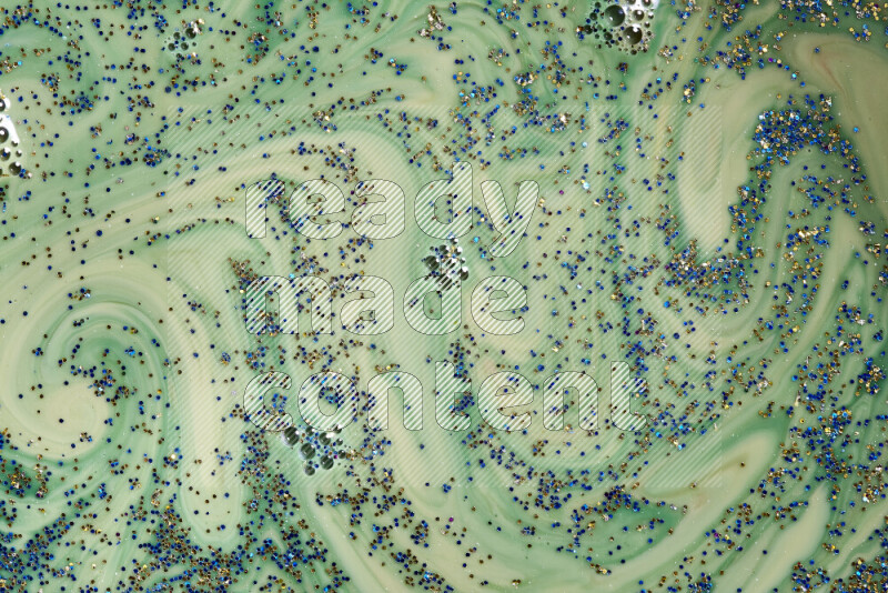 A close-up of sparkling blue and gold glitter scattered on swirling green background